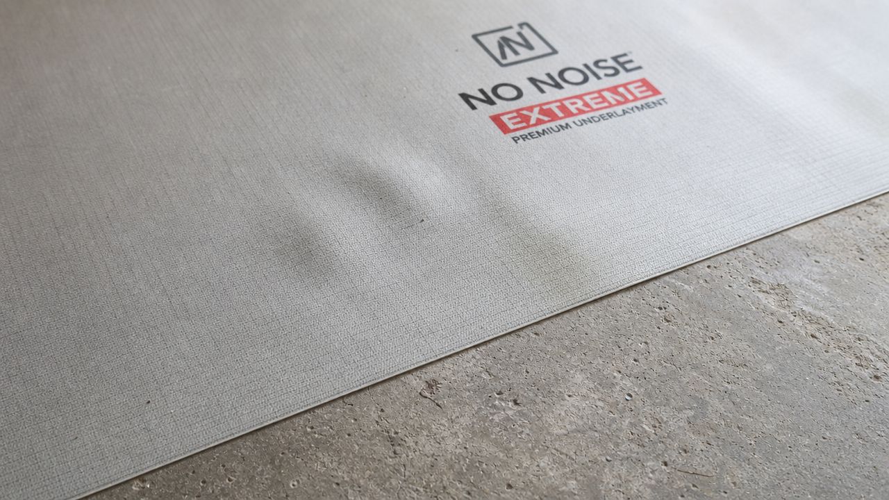Et tæt billede af No Noise Extreme underlagsmateriale med en tydelig ujævnhed placeret på et betongulv.
