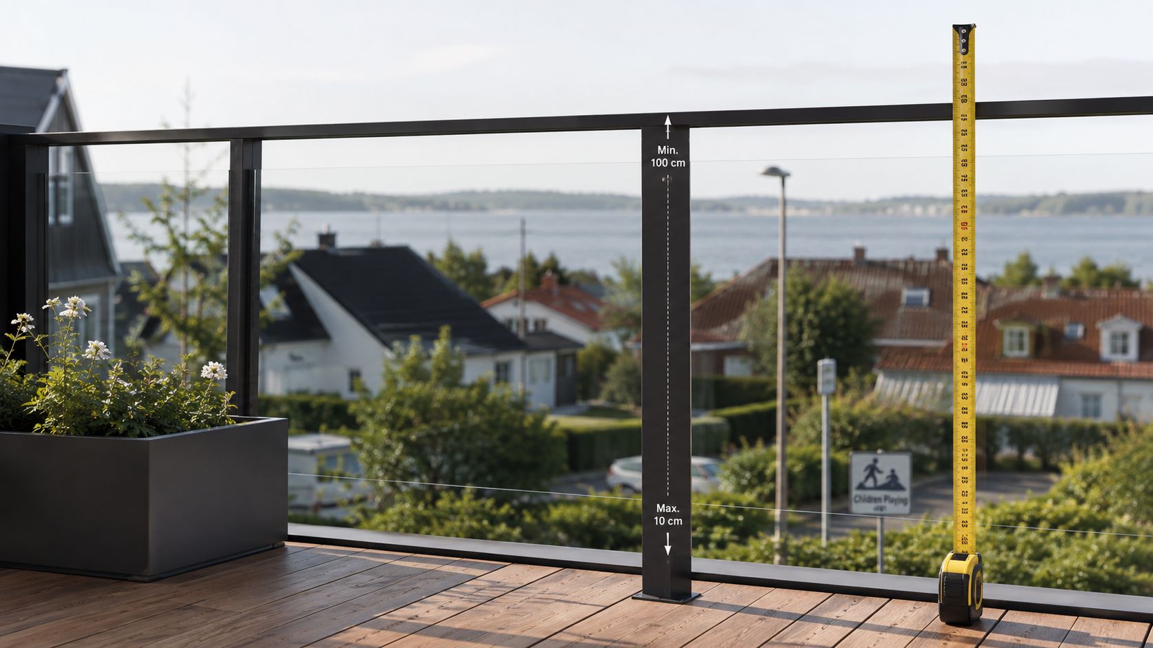 Et moderne terrasse gelænder i sort metal med glaspaneler og et målebånd der viser sikkerhedshøjden.